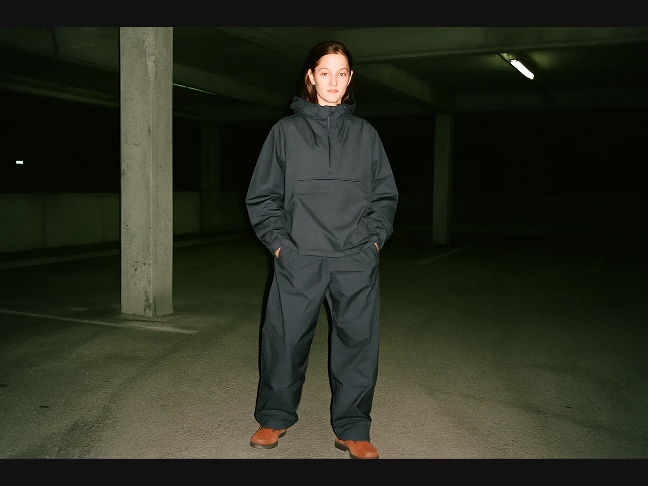 Model wearing charcoal technical streetwear in a concrete parking garage