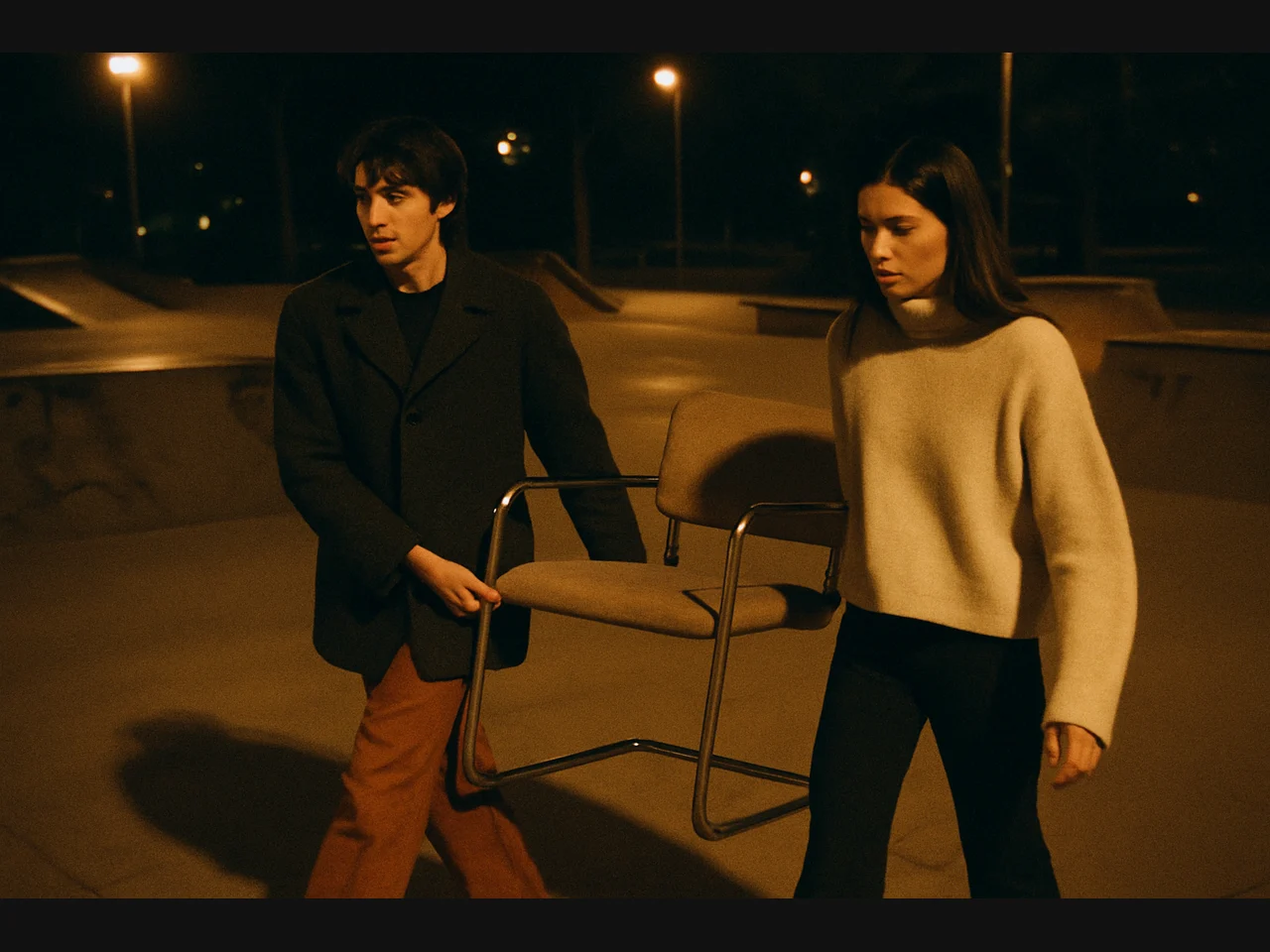 Two people carrying a tubular chair through a skatepark at night